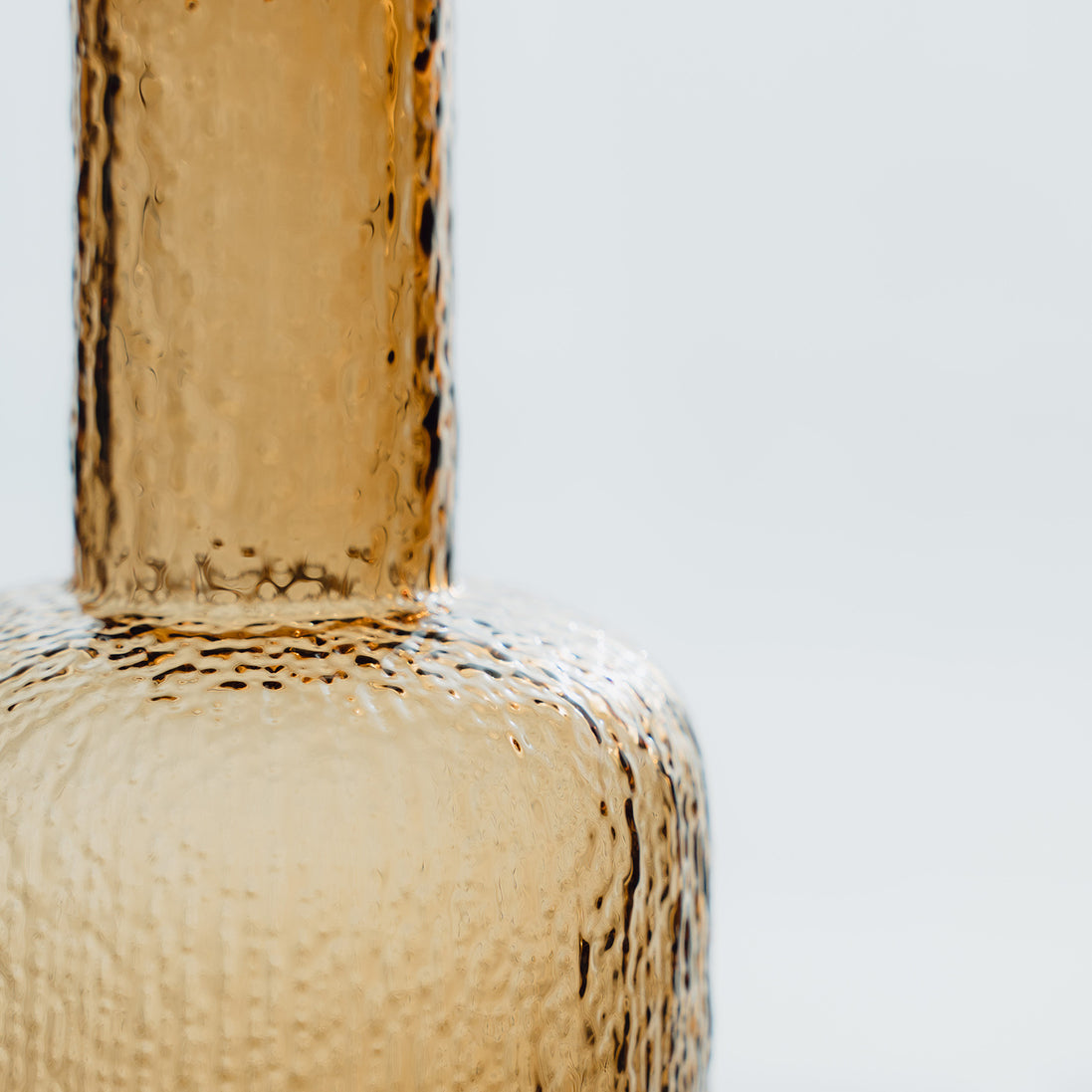 Hand-blown amber glass bottle with an ice-textured finish and rounded stopper for mid-century and contemporary luxury interiors.