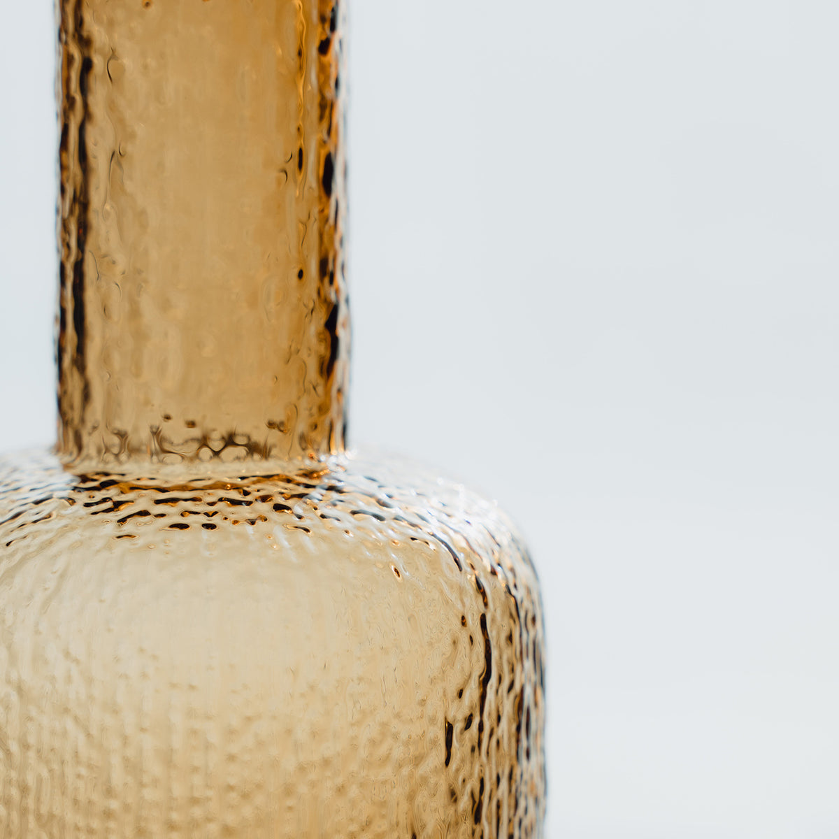 Hand-blown amber glass bottle with an ice-textured finish and rounded stopper for mid-century and contemporary luxury interiors.