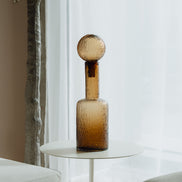 Hand-blown amber glass bottle with an ice-textured finish and rounded stopper for mid-century and contemporary luxury interiors.