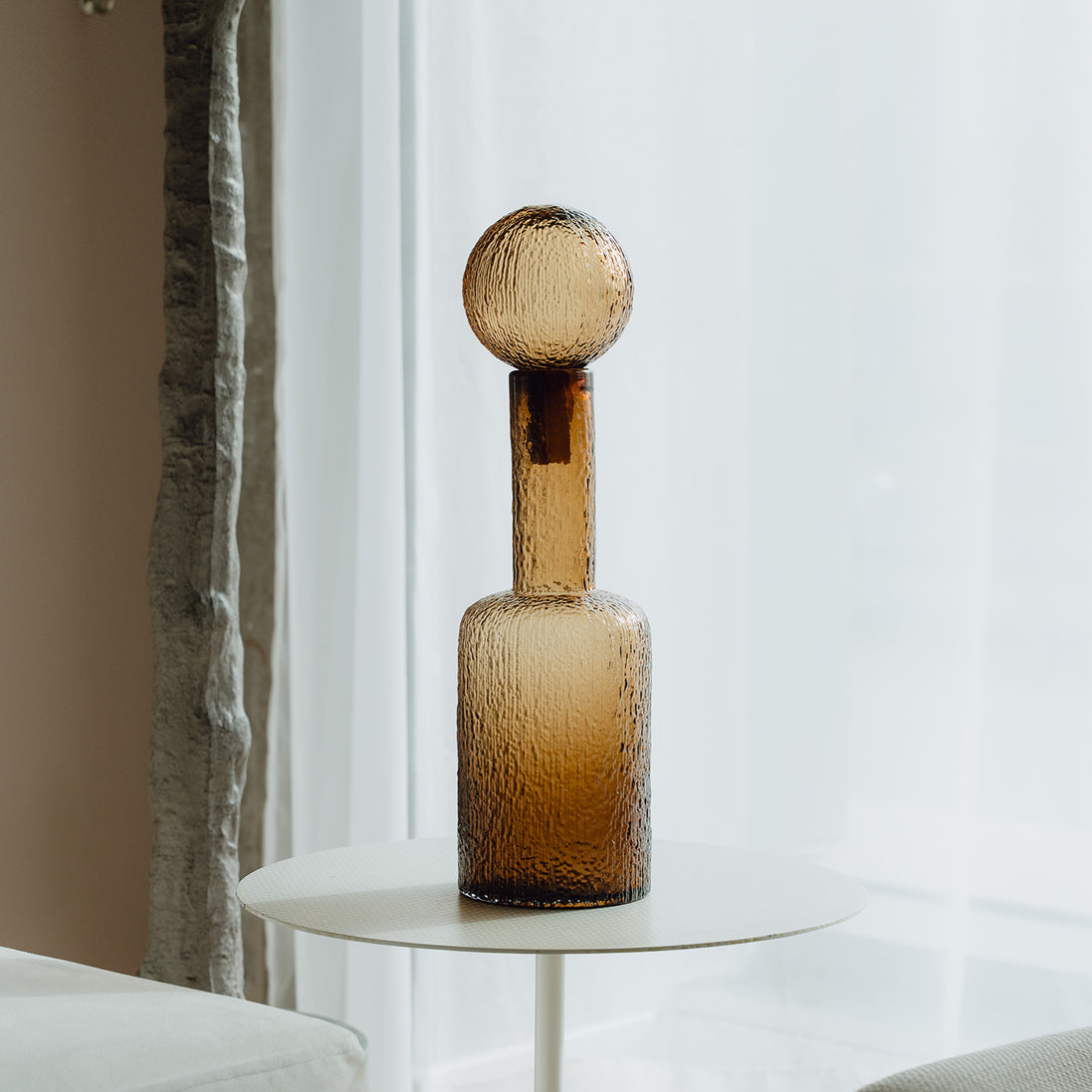 Hand-blown amber glass bottle with an ice-textured finish and rounded stopper for mid-century and contemporary luxury interiors.