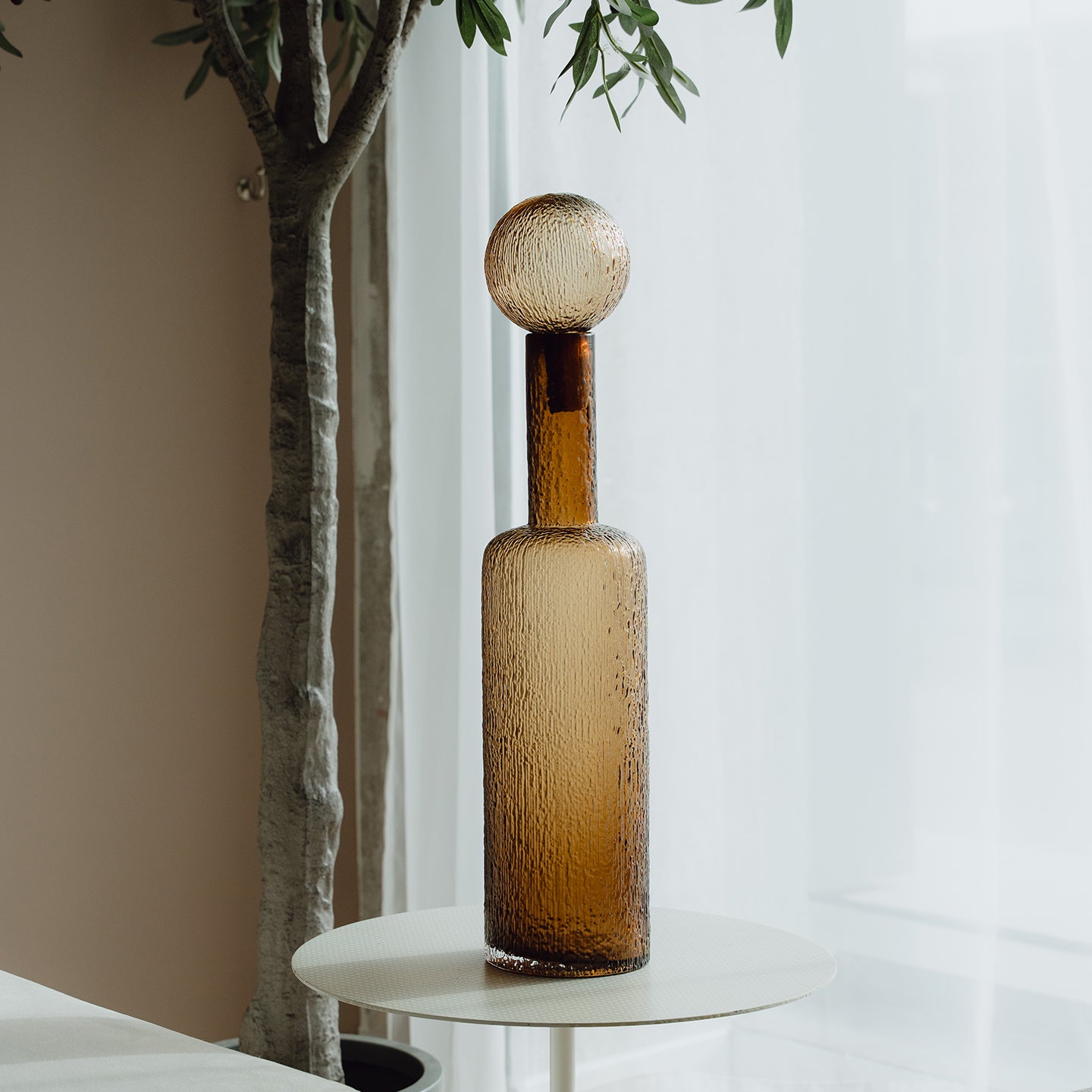 Hand-blown amber glass bottle with an ice-textured finish and rounded stopper for mid-century and contemporary luxury interiors.