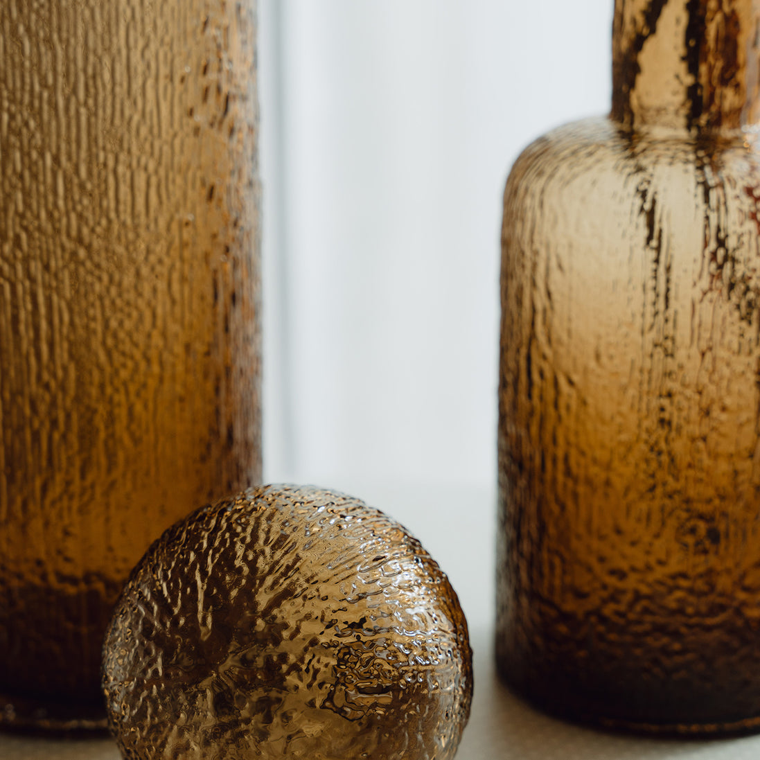 Hand-blown amber glass bottle with an ice-textured finish and rounded stopper for mid-century and contemporary luxury interiors.