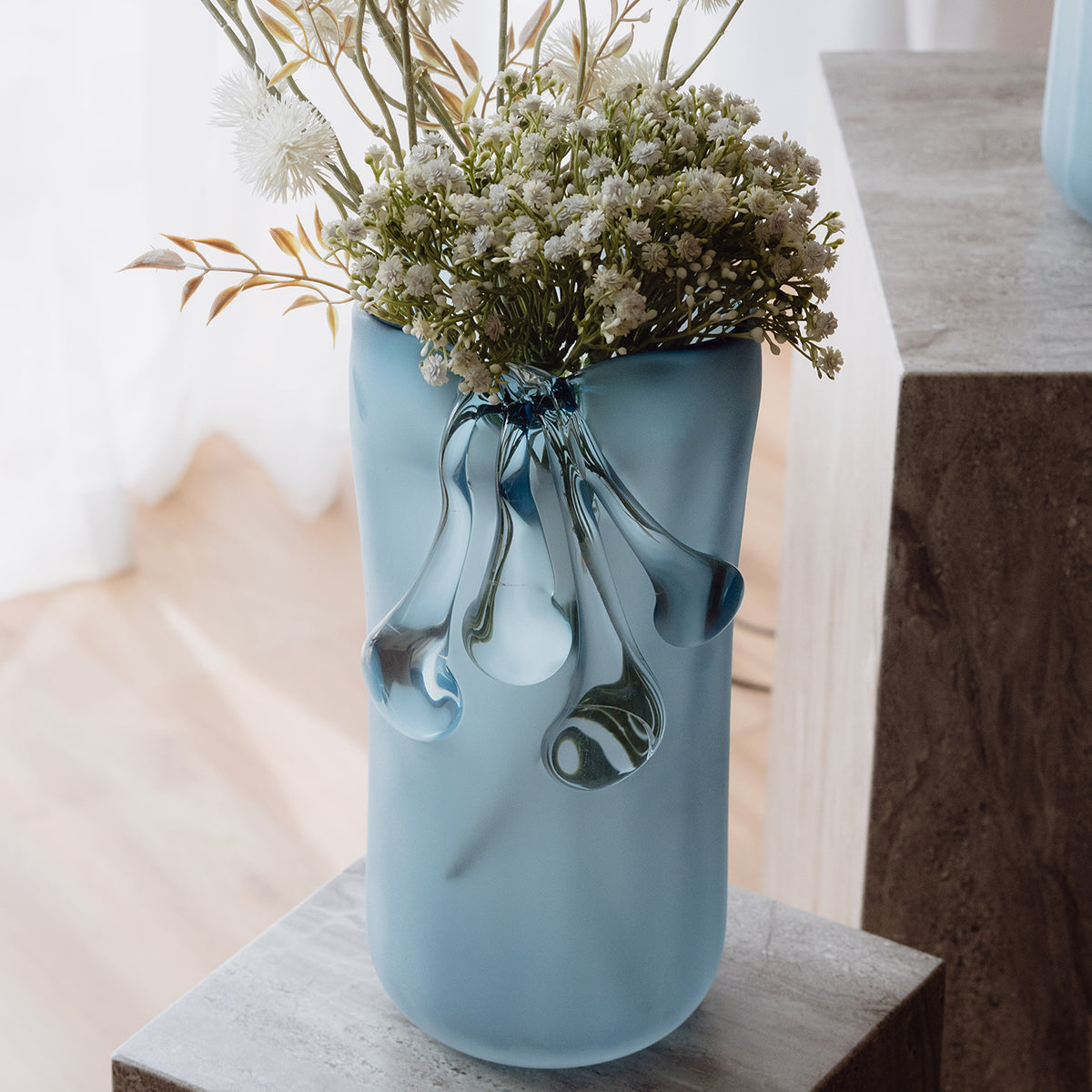 Frosted light blue decorative glass vase with a sculptural flowing silhouette for contemporary and luxury interiors.