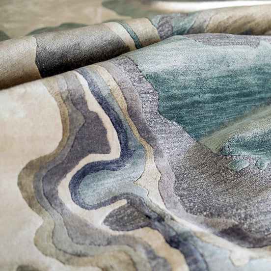 Handmade bamboo silk rug with textured organic motifs in soft blue, deep green, and neutral tones inspired by flowing water.