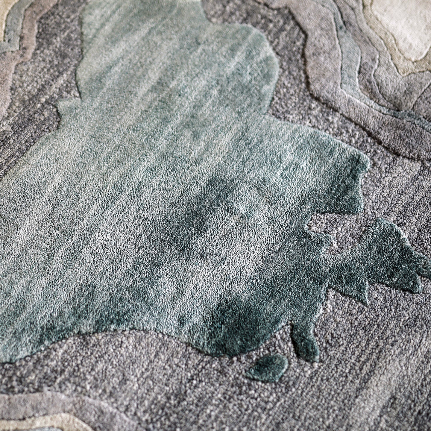 Handmade bamboo silk rug with textured organic motifs in soft blue, deep green, and neutral tones inspired by flowing water.