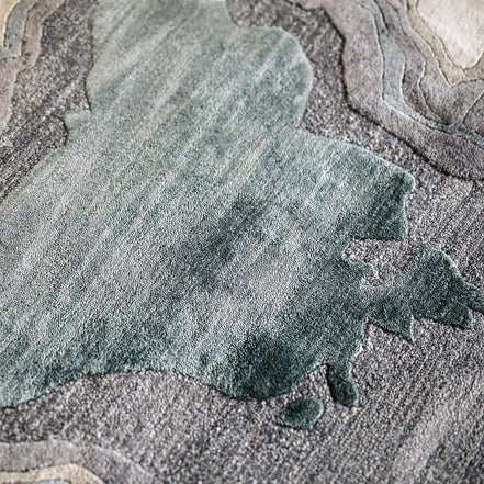 Handmade bamboo silk rug with textured organic motifs in soft blue, deep green, and neutral tones inspired by flowing water.