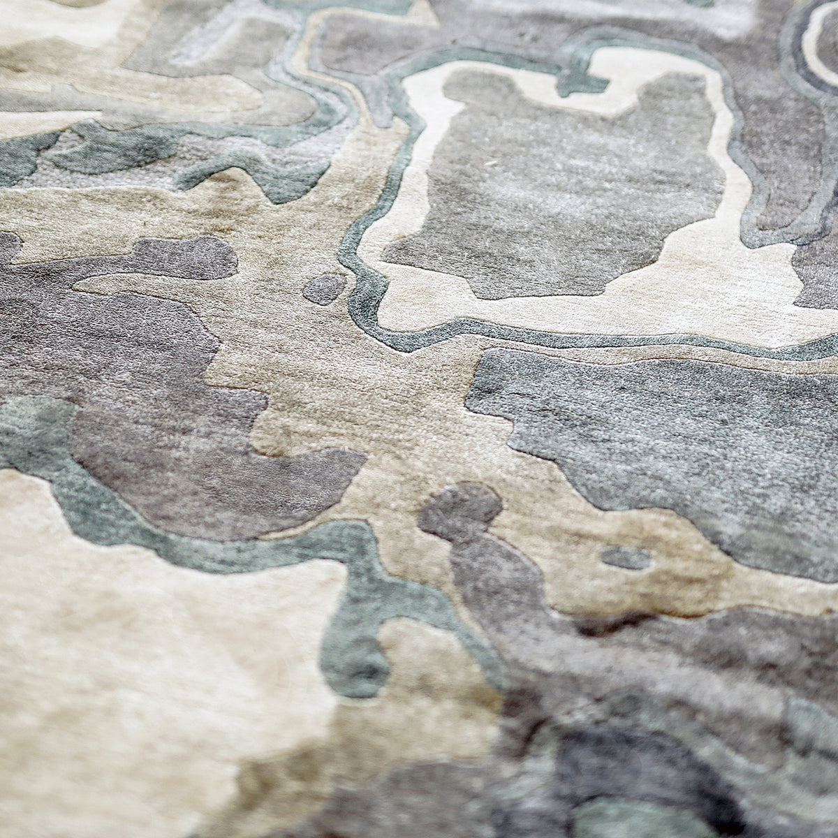 Handmade bamboo silk rug with textured organic motifs in soft blue, deep green, and neutral tones inspired by flowing water.