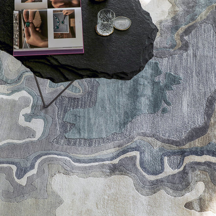 Handmade bamboo silk rug with textured organic motifs in soft blue, deep green, and neutral tones inspired by flowing water.