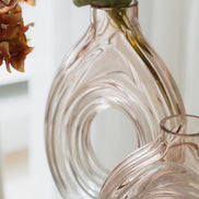 Hand-blown blush glass vase with a sculptural spiral design and flattened silhouette, available in two sizes for modern luxury interiors.
