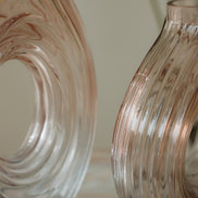 Hand-blown blush glass vase with a sculptural spiral design and flattened silhouette, available in two sizes for modern luxury interiors.