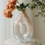 Hand-blown blush glass vase with a sculptural spiral design and flattened silhouette, available in two sizes for modern luxury interiors.