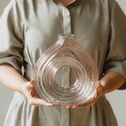 Hand-blown blush glass vase with a sculptural spiral design and flattened silhouette, available in two sizes for modern luxury interiors.