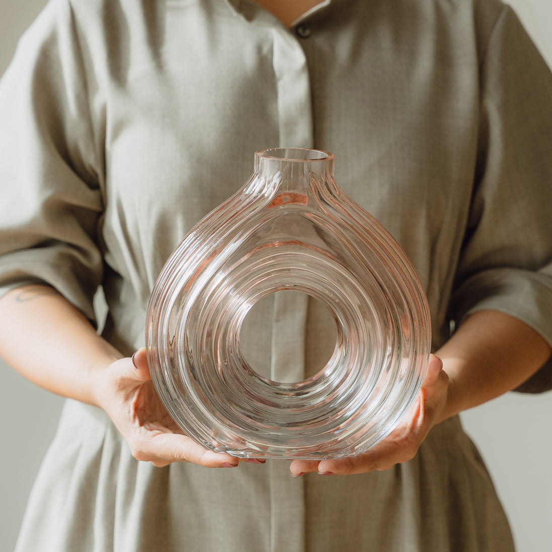 Hand-blown blush glass vase with a sculptural spiral design and flattened silhouette, available in two sizes for modern luxury interiors.