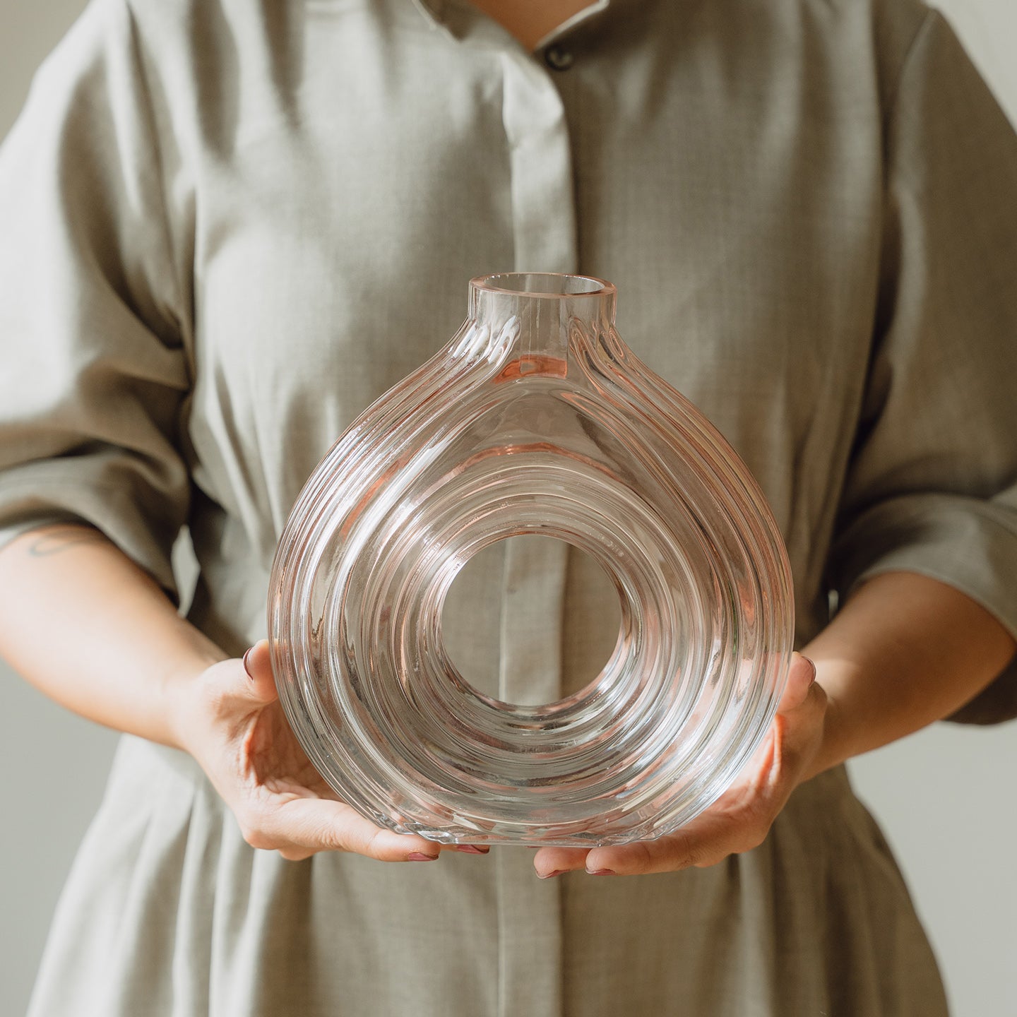 Hand-blown blush glass vase with a sculptural spiral design and flattened silhouette, available in two sizes for modern luxury interiors.