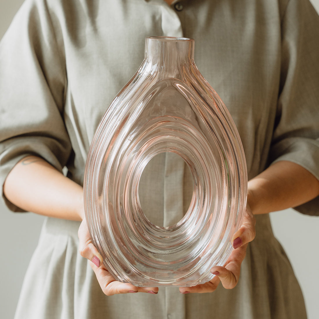 Hand-blown blush glass vase with a sculptural spiral design and flattened silhouette, available in two sizes for modern luxury interiors.