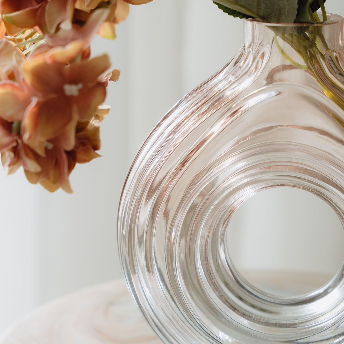 Hand-blown blush glass vase with a sculptural spiral design and flattened silhouette, available in two sizes for modern luxury interiors.