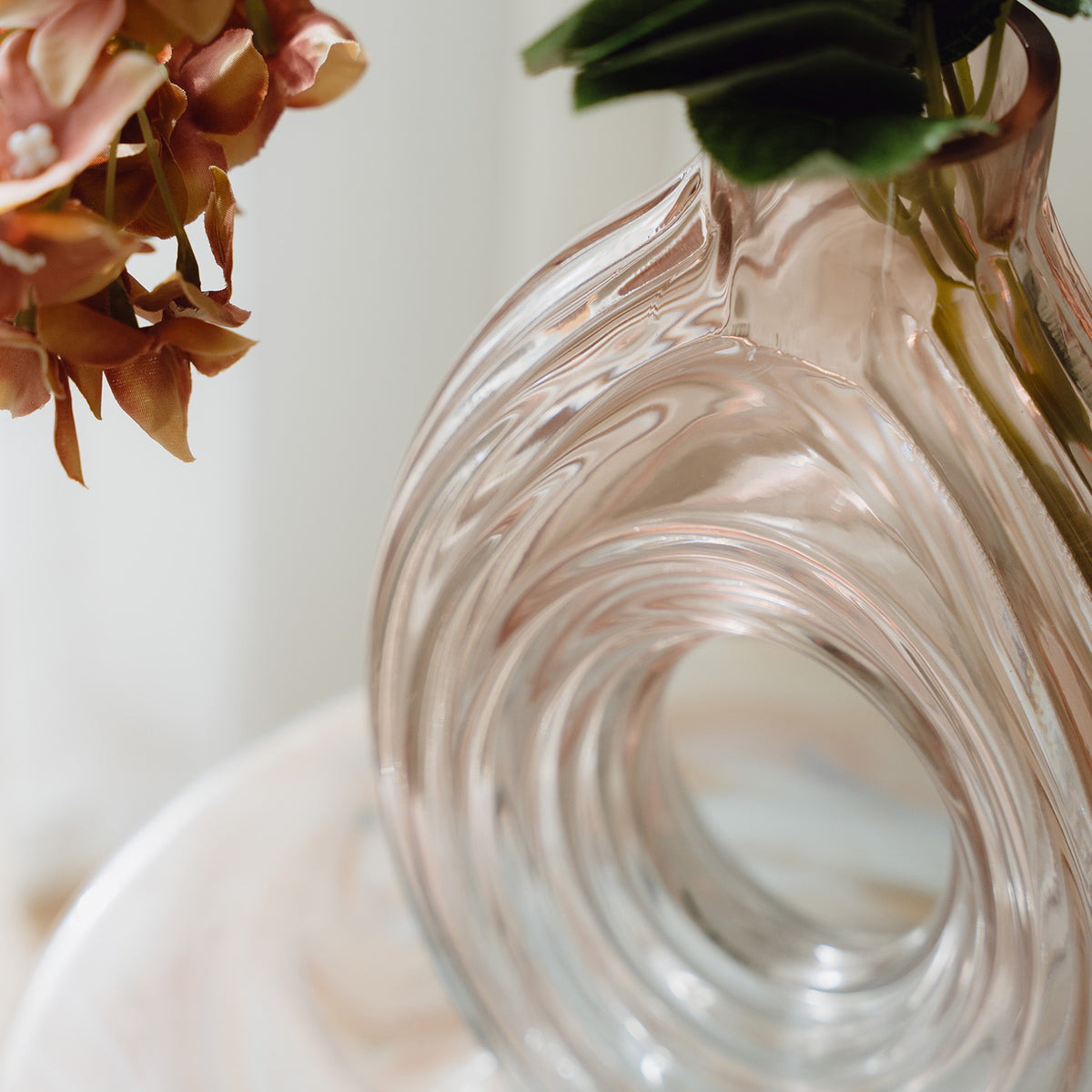 Hand-blown blush glass vase with a sculptural spiral design and flattened silhouette, available in two sizes for modern luxury interiors.