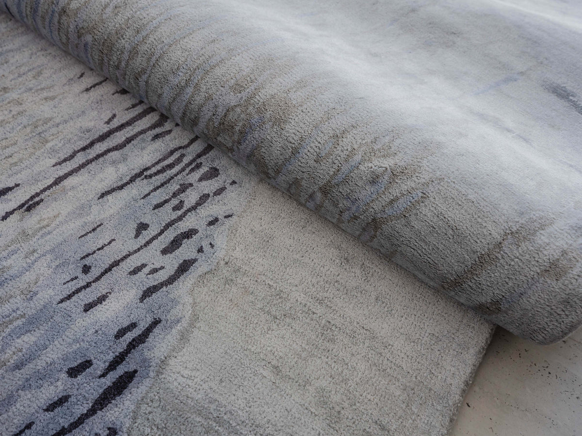 Handmade abstract rug inspired by blue stone and ocean waves with a flowing wave pattern, soft sheen, and velvety texture.