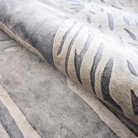 Handmade silver-grey rug with raised ivory abstract patterns and a textured finish for contemporary luxury interiors.