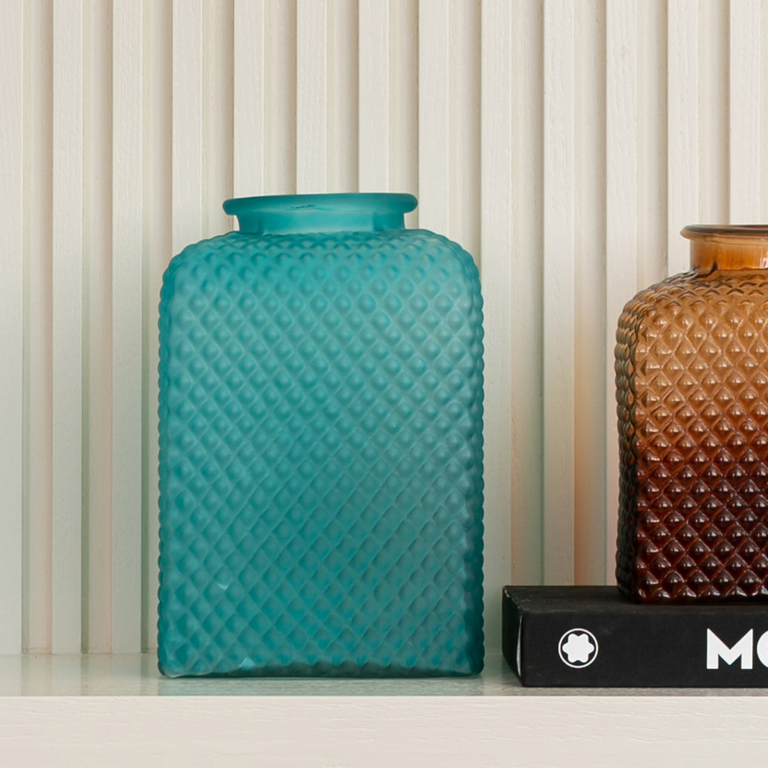 Discover the Speckle Textured Glass Vase in light blue or amber, featuring a sculptural shape and light-catching speckled finish. Available in two sizes.